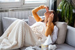 © Graphicroyalty - Young woman using nasal spray on sofa. Sick girl with blocked nose treating sinus congestion with spray while wrapped in blanket. Allergy and rhinitis relief concept with tissue box on the couch.