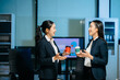 © Nuttapong punna - Two businesswomen having a friendly discussion during coffee break in modern office. Professional teamwork, collaboration, communication, startup and corporate workplace lifestyle.