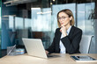 © Liubomir - Professional businesswoman wearing glasses and a formal suit, sitting at a desk and focusing intently on her laptop screen, demonstrating dedication and efficiency in a modern corporate workspace