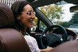 © Westend61 - Smiling young woman driving convertible car in city