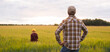 © Acronym - Farmer and his son in front of a sunset agricultural landscape. Man and a boy in a countryside field. Fatherhood, country life, farming and country lifestyle concept.