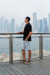 © Studio Peace - Man looking at city skyline from pier. Urban view with modern towering buildings. Dubai Marina.