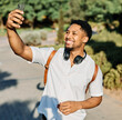 © Lumos sp - Young man enjoys sunny day while using smartphone and listening to music with earphones ant taking a selfie  in urban setting, highlighting his joy and connection to the world around him