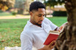 © Lumos sp - Young man student businessman enjoys sunny day while reading a book in park, highlighting his joy and connection to the world around him