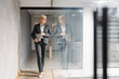 © Novak - Confident middle-aged businesswoman walking through a modern office hallway with a laptop.