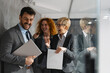© Novak - A group of diverse professional business people leaving a modern office building after work. They are walking together, smiling, and engaging in a friendly conversation