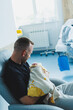 © DSMT - Young father holds his newborn baby in his arms while sitting in the delivery room. The first minutes after the birth of the baby in the maternity hospital. Young father loves and hugs his baby.