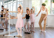 © JackF - Adult woman teacher helping group of girls dancers practicing plie movement at barre in studio
