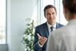 © Stitch - A friendly male financial advisor in a suit gesturing as he explains investment options to a client in a bright office.