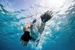 © Stitch - An underwater shot of a man swimming in clear blue water, with sunlight creating bubbles.