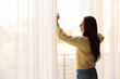 © New Africa - Beautiful woman opening window curtains at home