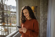 © Miljan Živković - Woman messaging on smart phone by window connecting online
