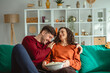 © Miljan Živković - Happy couple relaxing on sofa watching a movie and laughing