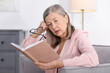© New Africa - Unhappy senior woman with book feeling fatigue at home