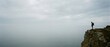 © Lianlian Liang - Man standing on edge of rocky cliff looking at foggy horizon symbolizing challenge and future vision