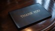 © Mudassir - Elegant black leather check presenter folder embossed with gold lettering saying thank you resting upon a richly polished dark wood table surface in a fine dining setting