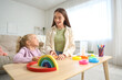 © Pixel-Shot - Nanny and cute little girl playing with toys on table at home