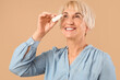 © Pixel-Shot - Mature woman using eye drops on beige background