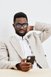 © SHOTPRIME STUDIO - Stylish young man wearing glasses and beige blazer using smartphone while sitting at table against plain white background. People lifestyle concept, modern, casual, social media, communication, urban.