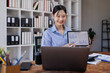 © David - Asian businesswoman pointing at a tablet screen showing Report graph financial data to her colleague during a working meeting online at desk.