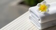 © antuanetto - A stack of soft white towels topped with a delicate plumeria flower for a tropical spa relaxation concept and serene rest