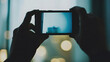 © Aliaksandr - Silhouette of hands holding a smartphone and taking a photo of the city at night. Mobile photography concept with bokeh lights background.