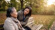 © Fernando - Asian senior woman talking with younger Asian woman on park bench in autumn, caregiver or family support, warm conversation, golden hour light