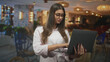 © Krakenimages.com - Woman with glasses typing on a laptop, holding it with visible hands in a cafe interior while looking at the screen; concentration productivity.