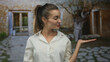 © Krakenimages.com - Young hispanic woman in white shirt holds out hand palm up at rustic house entrance framed by stone courtyard; friendly invitation.
