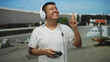© Krakenimages.com - Young hispanic man with headset holds game controller and points finger upward in airport terminal; joyful play.