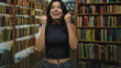 © Krakenimages.com - Woman pumping fists among bookshelves in library while wearing navy top and jeans, smiling broadly; excitement.