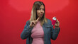 © Krakenimages.com - Woman holds a pink toothpaste bottle and points her index finger while looking skeptical against a red studio backdrop, wearing denim jacket; doubt.