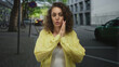 © Krakenimages.com - Woman with hands covering mouth and palms raised on a city street wearing yellow shirt, frontal; surprise reaction.