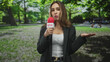 © Krakenimages.com - Woman reporter holds red microphone and gestures open palm on street; live location reporting serious.