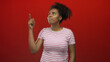 © Krakenimages.com - Woman points index finger upward in studio with red backdrop, wearing white tee with pink stripes and looking up; curiosity reflection.