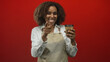 © Krakenimages.com - Young woman in apron smiling and pointing finger at a takeaway coffee cup in a red studio; happiness warmth.