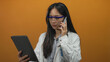© Krakenimages.com - Scientist woman in lab coat and safety glasses on phone using tablet against orange wall.
