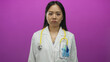 © Krakenimages.com - Young chinese woman doctor with stethoscope stands in uniform against isolated pink background wall showing serious expression suggesting focus and professionalism.