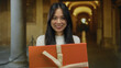 © Krakenimages.com - Woman smiling with a gift outdoors at an old university campus with columns and arches in the background.