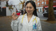 © Krakenimages.com - Young chinese woman doctor with stethoscope holding heart outdoors on street, symbolizing care and compassion in urban healthcare setting during day.