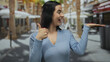 © Krakenimages.com - Hispanic woman outdoor giving thumbs up with palm extended in an urban street setting wearing blue smiling under palm trees in a sunny atmosphere.