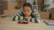 © Krakenimages.com - Woman resting on a table in a new home surrounded by boxes and looking at a smartphone, suggesting a mix of anticipation and fatigue in an indoor setting.