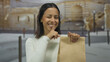 © Krakenimages.com - Hispanic woman gesturing quiet with finger on lips, holding brown paper bag outdoors in urban setting with blurred background, showcasing secrecy and mystery.