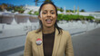 © Krakenimages.com - Young woman with hispanic descent stands proudly outdoors wearing a badge reading 'i voted' with an american flag theme, symbolizing civic engagement on a sunny street.