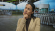 © Krakenimages.com - Woman in thoughtful pose at an airport terminal with outdoor setting, captured amidst trolleys, reflecting travel anticipation.