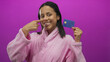 © Krakenimages.com - Woman in bathrobe holding credit card smiles confidently against vibrant pink background symbolizing financial freedom and modern lifestyle.