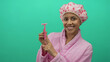 © Krakenimages.com - Hispanic woman in a pink bathrobe and shower cap holding a pink razor against a green background, smiling confidently at the camera.