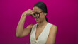 © Krakenimages.com - Hispanic woman with glasses expressing concern against a vibrant pink background, holding her head in a thinking or headache gesture, wearing a casual white top.