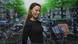 © Krakenimages.com - Young woman smiling with hands behind back and visible face on street in amsterdam by bicycles and canal; playful spontaneity.