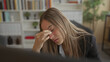 © Krakenimages.com - Woman pinches nose bridge at office desk, leaning toward a computer with bookshelf and plant in the room; work fatigue.